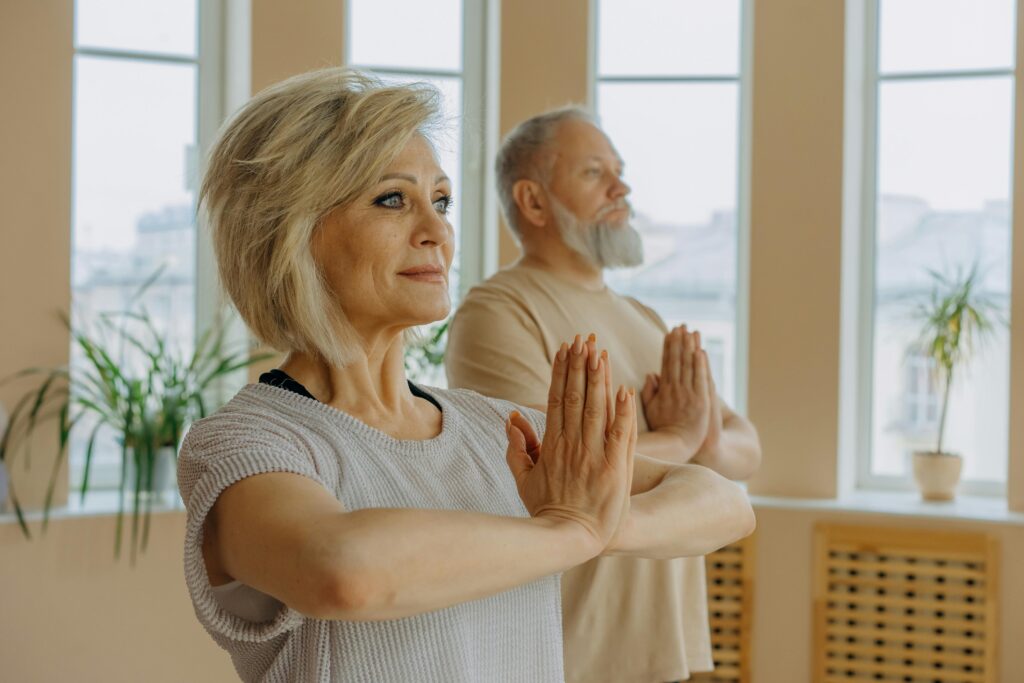 Elderly man and woman engaged in yoga indoors, promoting healthy lifestyle.